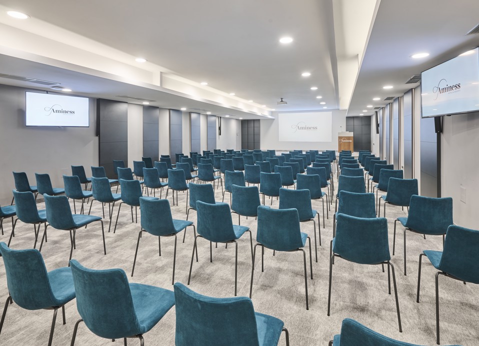 The image shows the Maestral conference room, photographed from behind, with the stage in the front.