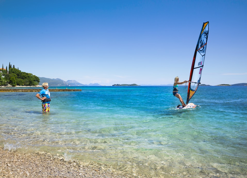 Windsurfer klizi preko mirnog mora s slikovitom planinskom pozadinom blizu Aminess Vival Grand Azur Hotela.