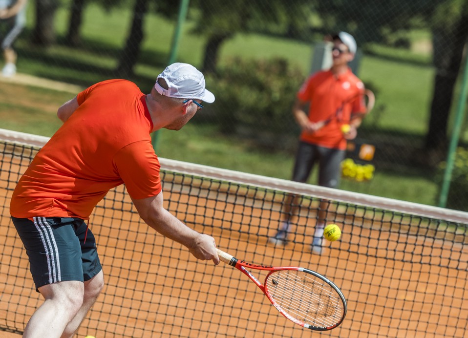 Un uomo che pratica il tennis con un allenatore sullo sfondo.