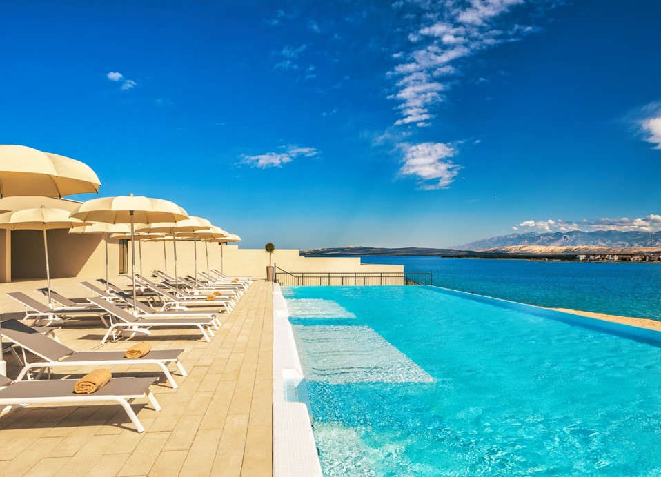 Sedie a sdraio e ombrelloni allineati accanto alla piscina relax con vista mare presso il resort Aminess Style Camping Avalona.