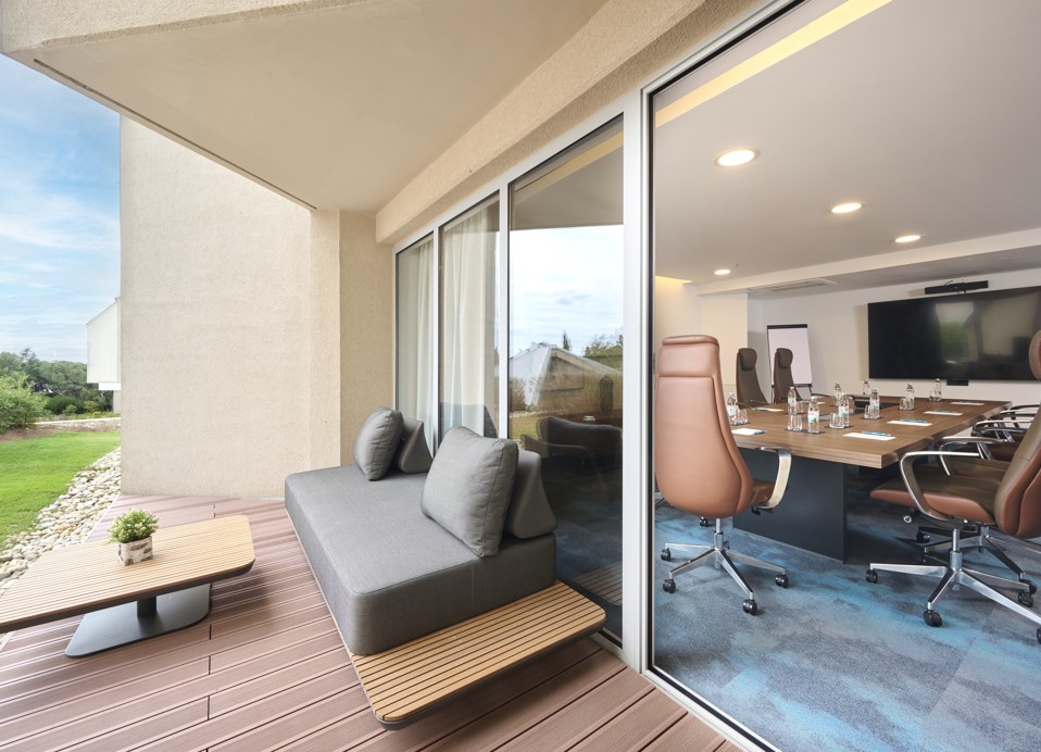 The image shows the Burin conference room, set up for a meeting, with an outdoor terrace featuring a table, couch, and greenery.