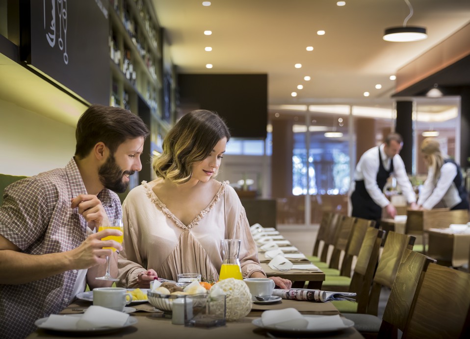 Een stel dat ontbijt in het Ventola restaurant, met een ober die tafels dekt op de achtergrond.