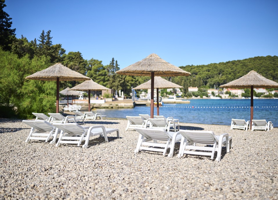 Sonnenliegen mit Sonnenschirmen am Kieselstrand, die im Aminess Vival Port9 Resort in Korcula Schatten vor der Sonne bieten.