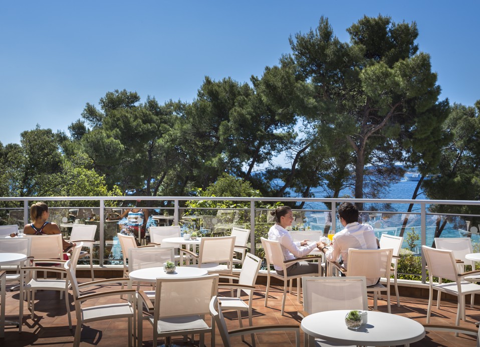 Gäste genießen Getränke an einer Terrassenbar mit dem Meer und Bäumen im Hintergrund im Aminess Vival Grand Azur Hotel.