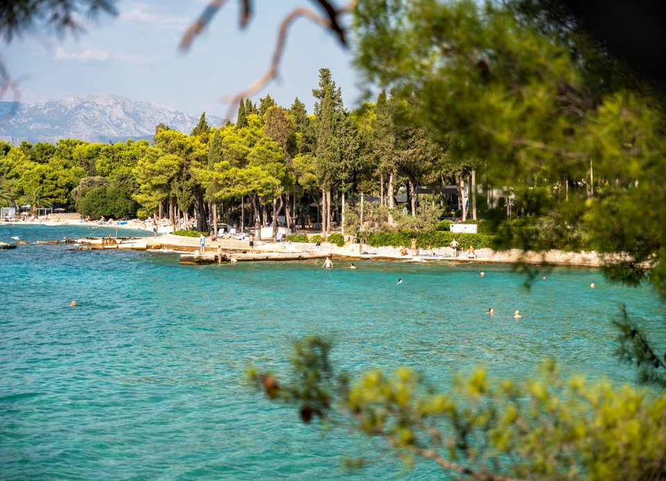 Sončna zaliv z kristalno čistim morjem in borovim gozdom pred Aminess Vival Velaris Resortom na otoku Braču – popolno mesto za sprostitev in uživanje v naravi med počitnicami na Hrvaškem.