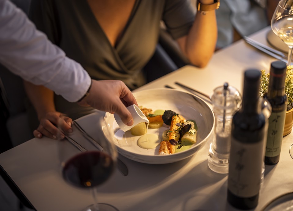 Elegantna izkušnja večerje v restavraciji 7 Seas v Aminess Style Camping Atea Resort, kjer postrežejo gurmansko jed s steklenicami vina in kozarci na mizi.