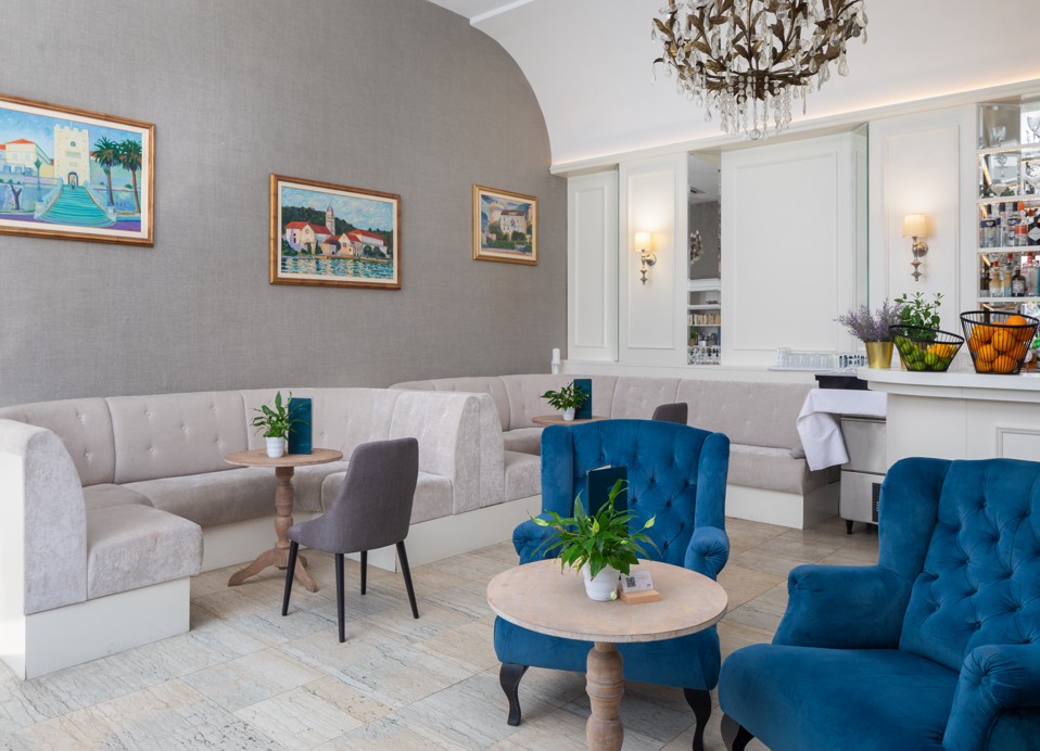 Interno del G&T lounge bar all'interno dell'Aminess Korcula Heritage Hotel, con un elegante arredamento in blu e grigio con poltrone lounge blu, lampadario di cristallo e decorazione murale.