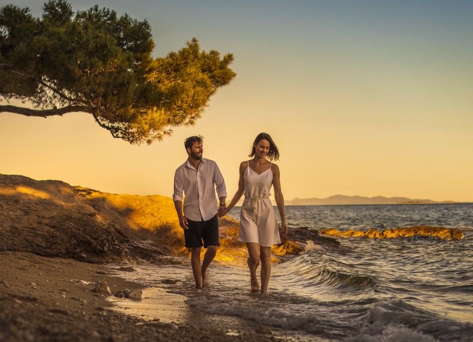 Romantični par se sprehaja ob plaži ob sončnem zahodu v Orebicu, Hrvaška, blizu Aminess Maradiso Bellevue Village.