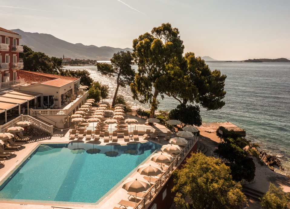Sonnenliegen befinden sich am Pool, Pinienbäume und ein Strand im Aminess Belleveu Hotel in Kroatien.