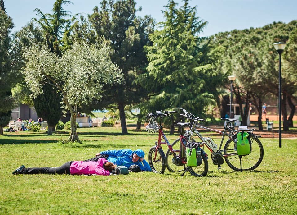 "Coppia anziana sdraiata sull'erba accanto alle loro biciclette presso l'Aminess Maradiso Hotel Laguna, Novigrad Croazia"