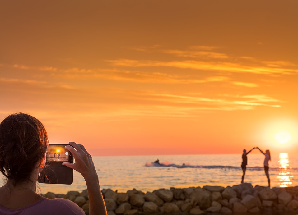 Frauen, die ein Foto von einem Paar machen, das auf den Felsen posiert, mit dem Sonnenuntergang im Hintergrund im Aminess Planet Camping Maravea Resort, Novigrad Kroatien