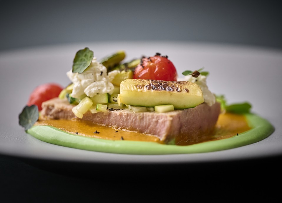 Cena raffinata di filetto di tonno con verdure grigliate colorate e condimenti su un piatto grigio all'interno dell'Aminess Younique Korcula Heritage Hotel.