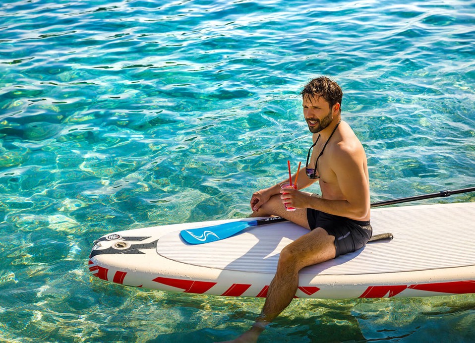 Mann sitzt auf einem Paddleboard mit einem Cocktail in der Hand bei Aminess Planet Camping Sirena in Novigrad, Kroatien