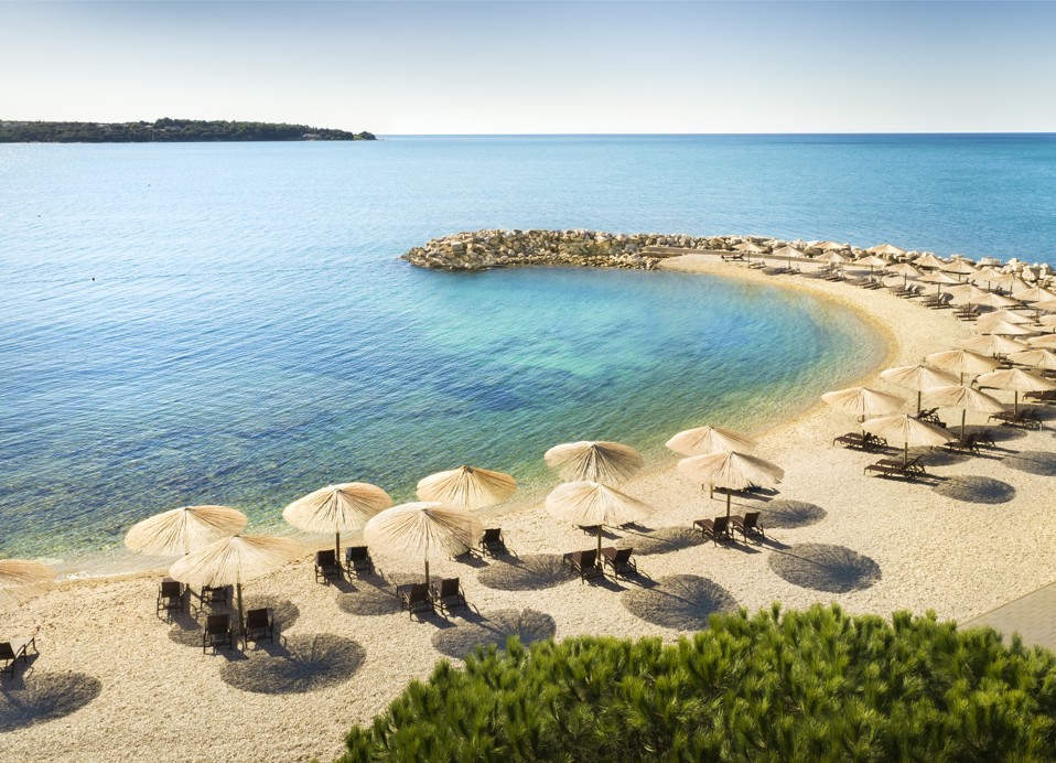 Dobro uređena šljunčana plaža s ležaljkama i suncobranima.