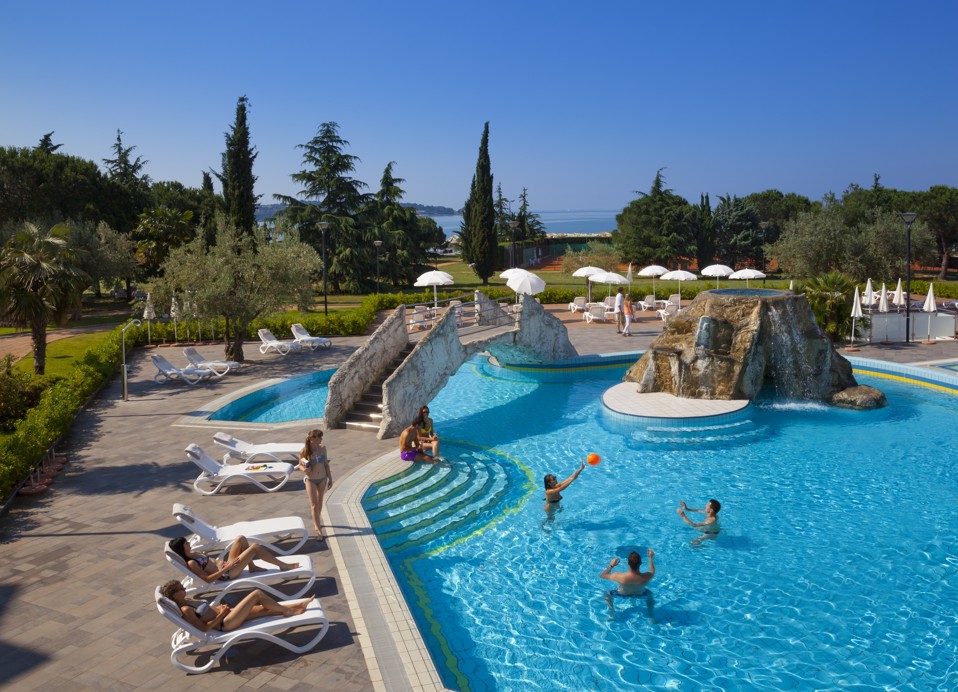 Vanjski bazen s ležaljkama, pogled na most i ljudi koji igraju odbojku u bazenu.