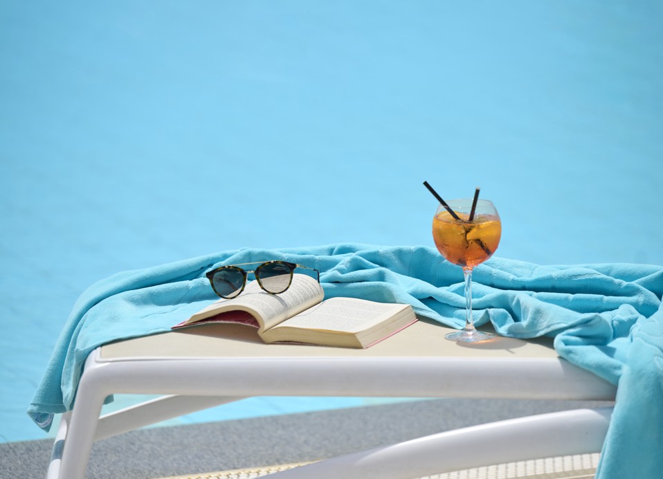 Cocktail, Buch und Sonnenbrille auf einer Liege am türkisfarbenen Pool im Hotel Lišanj.