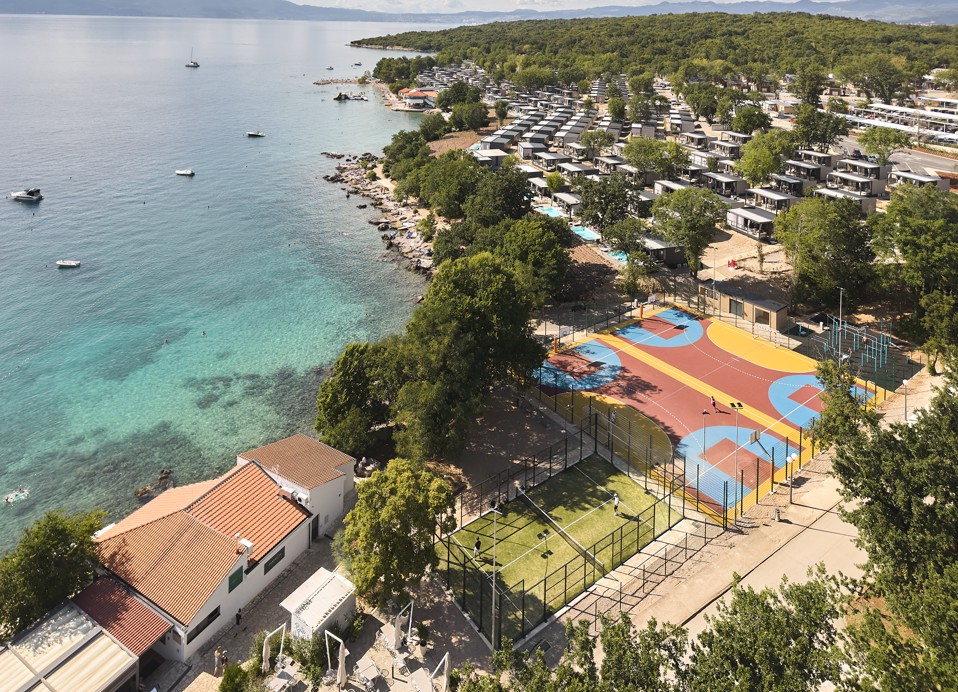 Blick auf das neue, lebendige Sportzentrum des Resorts, mit Plätzen umgeben von üppigem Grün und der ruhigen Adriaküste im Aminess Style Camping Atea Resort.