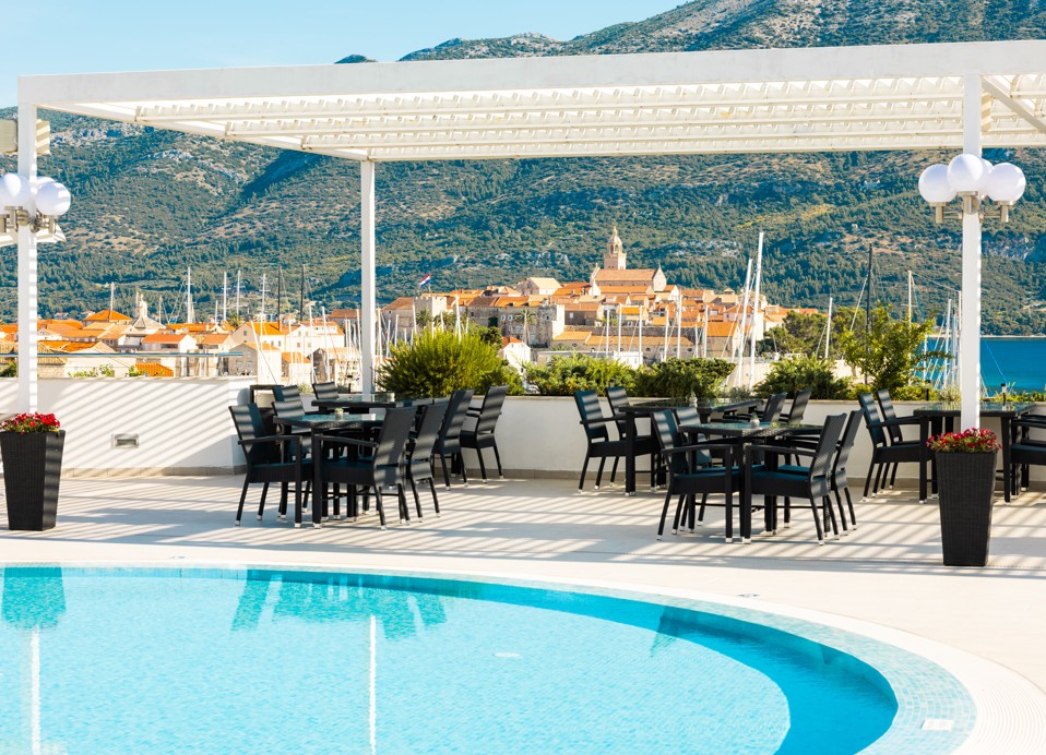 A wide-angle shot of the stylish aperitif bar in the lobby area, with a mix of comfortable seating, ambient lighting, and views of the coastline at the Maradiso Marko Polo by Aminess.
