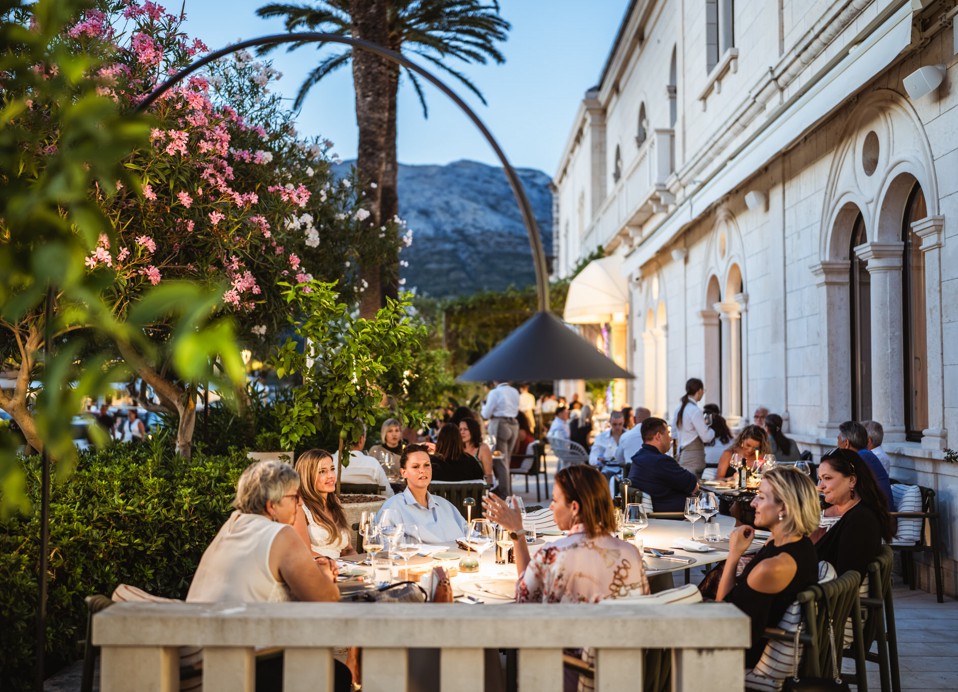Gostje večerjajo na terasi restavracije Aminess obdani z mediteranskim zelenjem.