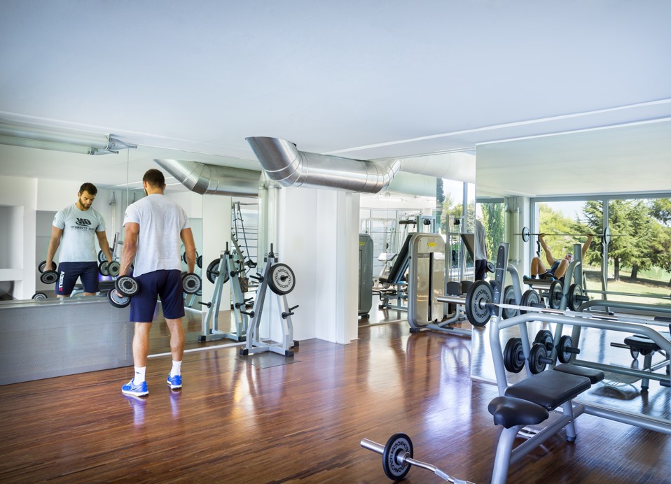 De afbeelding toont een rek met gewichten en een mannenhand die een dumbbell oppakt.