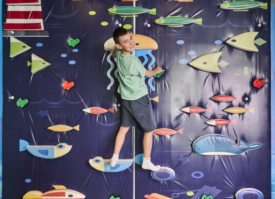 Jongen klimt op een indoor klimmuur met oceaanthema in een speelruimte