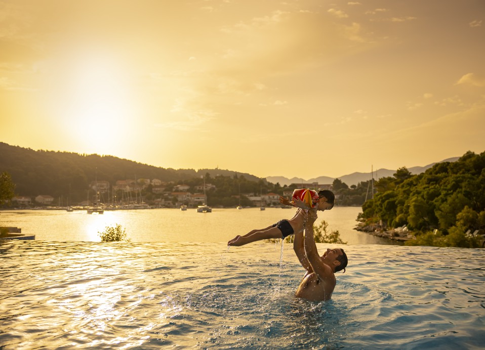 Ein Vater und Sohn genießen gemeinsame Zeit am Pool im Aminess Vival Port9 Resort mit einem atemberaubenden Sonnenuntergang auf der Insel Korcula in Kroatien