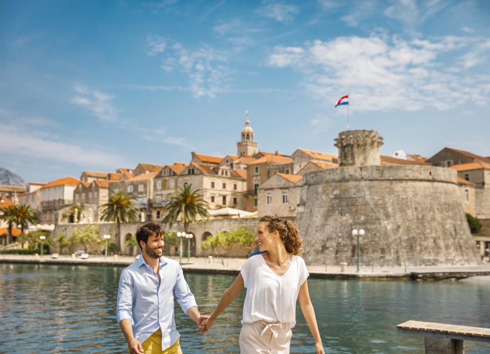 Koppel hand in hand voor de oude stad Korcula toren bij Spomenik strand in de buurt van het Aminess Younique Korcula Heritage Hotel.