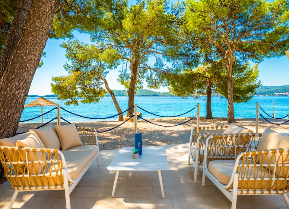 Außenbereich einer Bar und eines Restaurants mit Blick auf den Strand und Bäume im Aminess Vival Grand Azur Hotel.