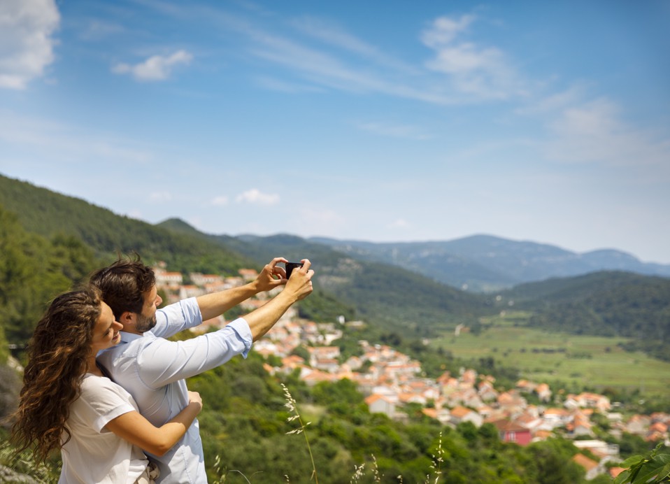 Scenic view of Cara Village with rolling hills, stone houses, and a guest enjoying the beautiful landscape.