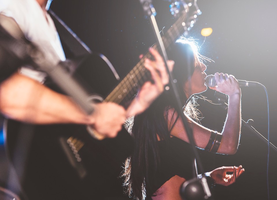 Live music performance featuring a singer and guitarist on a dimly lit stage, captivating the audience at the Maradiso Marko Polo by Aminess.