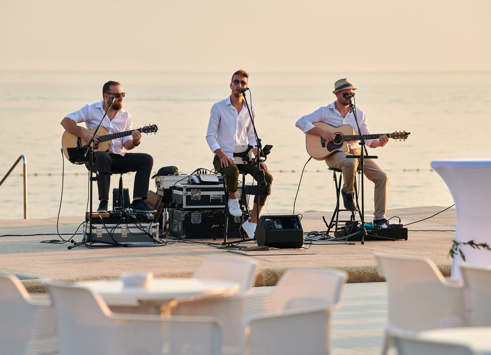 Wedding band performing on a lit stage, with the sea in the background.