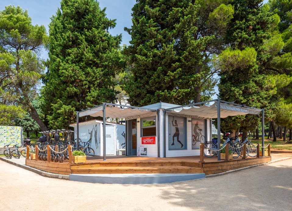 Centro sportivo che offre noleggio di biciclette e attrezzature con una vista panoramica sul mare sullo sfondo.